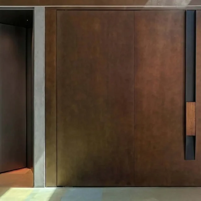 Main entrance door at Abyam House featuring a fully customized burnished bronze finish, a solid iroko wood pull handle, and an integrated Italian-engineered digital access system with multi-point locking by Silvelox, crafted by Metal Fabrik.