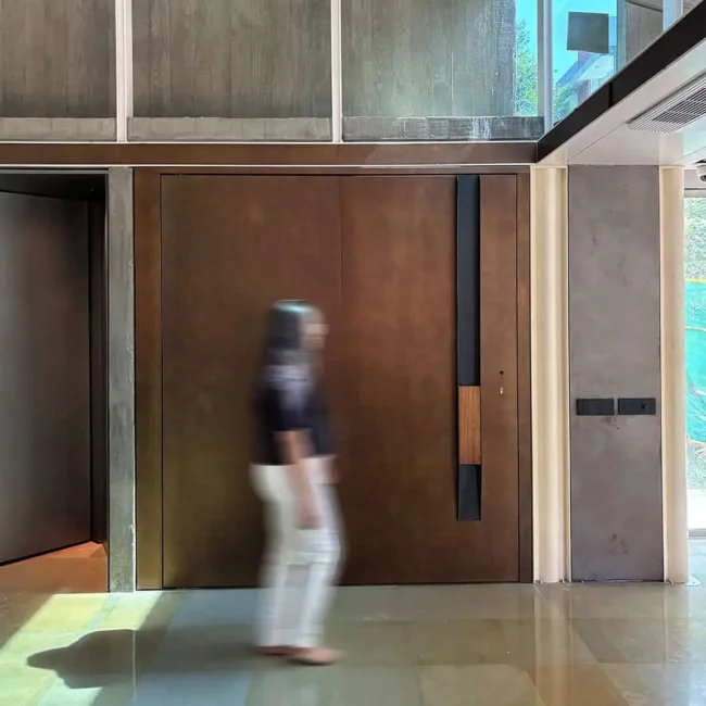 Architectural entrance door at Abyam House with custom burnished bronze cladding, iroko wood handle detail, and Italian-engineered multi-point digital locking system by Silvelox, produced by Metal Fabrik