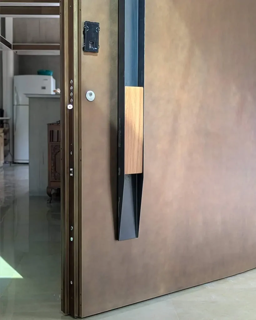 Abyam House front entrance door featuring bespoke burnished bronze finish, iroko wood handle, and integrated Italian-engineered smart locking system by Silvelox, crafted by Metal Fabrik.